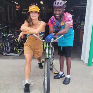 A man and woman pose with a bicycle they fixed and smile.