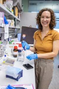 Dr. Emma Stapleton Thornell using a pipette on a lab bench and smiling.